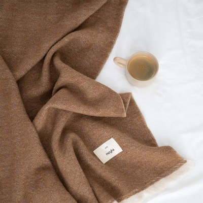 MOYHA Wolldecke Herringbone Haselnussbraun 130x170 cm auf einem Sofa