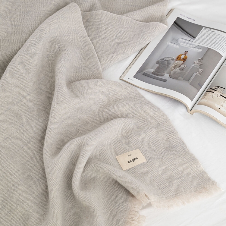 MOYHA Wolldecke Herringbone Hellgrau 130x170 cm auf einem Sofa